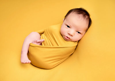 Baby boy wrapped in a yellow blanket taken at a newborn photoshoot in Hitchin
