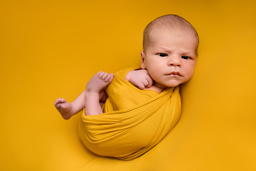 Baby boy wrapped in a yellow fabric wrap taken at a newborn photoshoot, Hitchin.