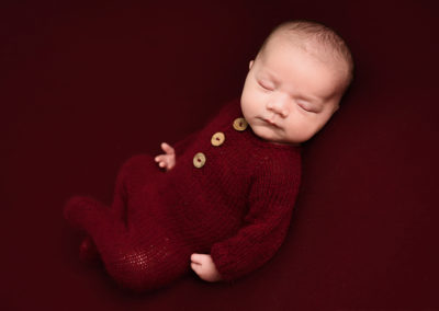 Baby boy wearing a red romper suit taken by Alice James Photography, newborn photographer Hertfordshire