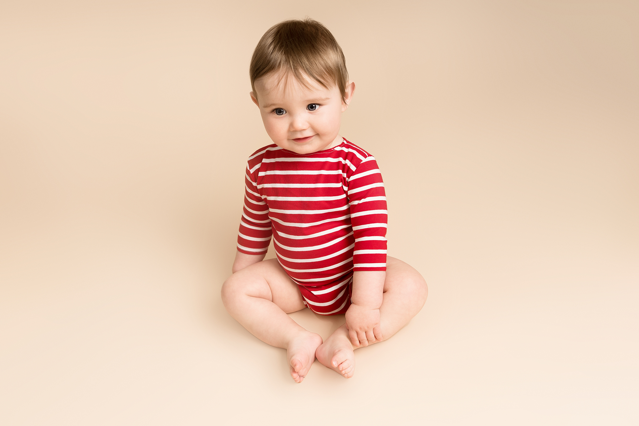 Baby boy wearing a red and white striped onesie at his baby photoshoots Hitchin.