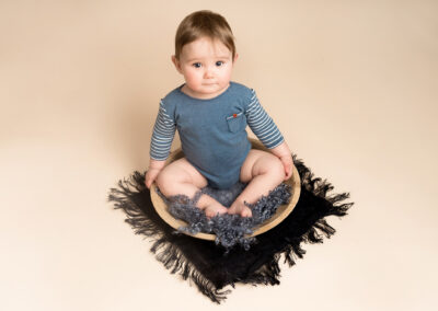 Baby boy wearing blue, sat in a wooden bowl. Taken by Alice James Photography, Baby photographer Hitchin