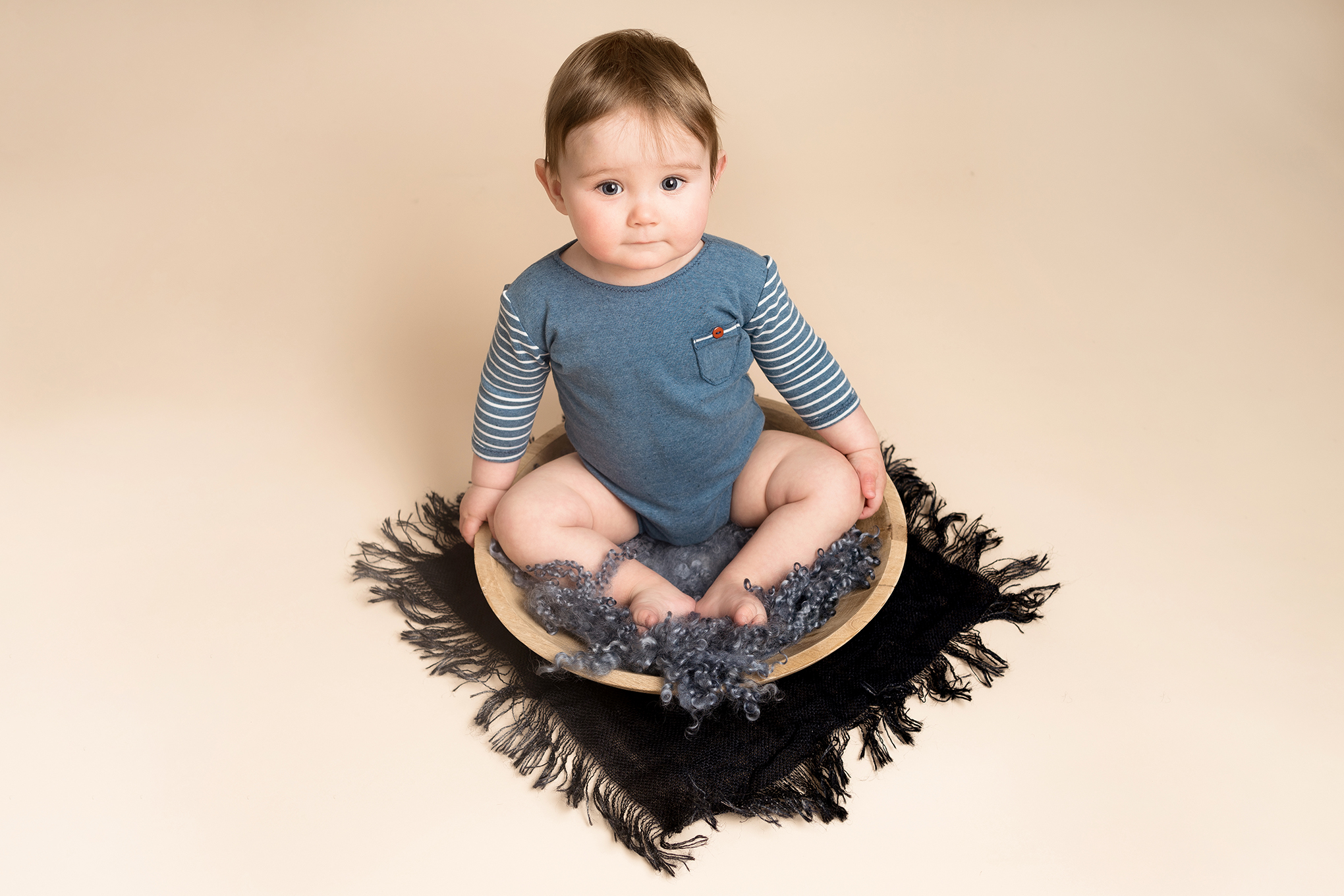 Baby boy wearing blue, sat in a wooden bowl at his baby photoshoot Hitchin