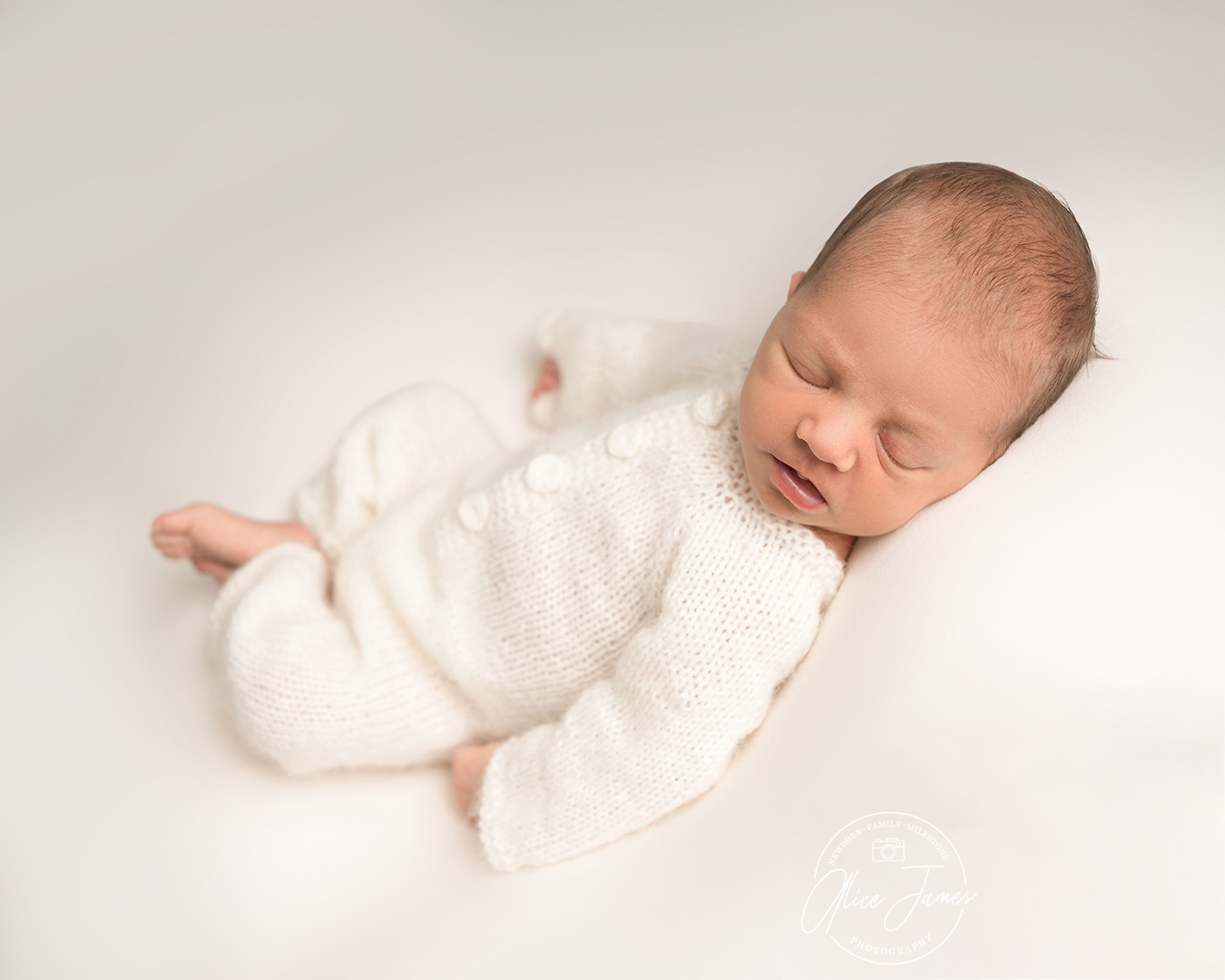 baby boy asleep at his newborn photoshoot Bedford. Wearing a cream knitted romper suit.