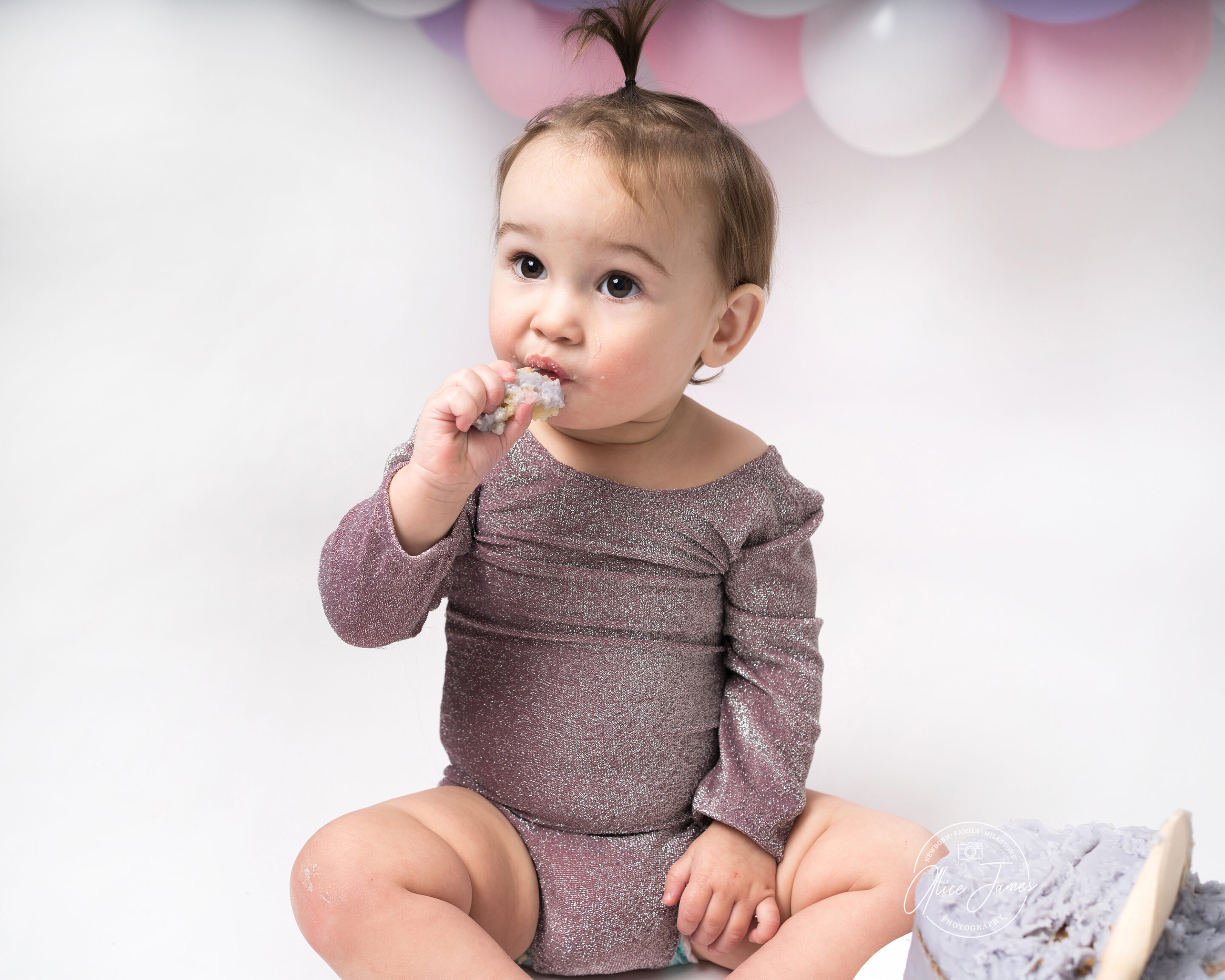 Baby girl eating cake off a wooden spoon. Taken at a cake smash photoshoot in Hitchin.